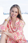 A long-haired blonde woman wearing a dress with a pink pattern