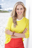 A long-haired blonde woman wearing a yellow top and red trousers