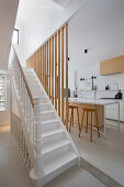 Staircase with white steps and wooden slats as partition to open-plan kitchen with island counter