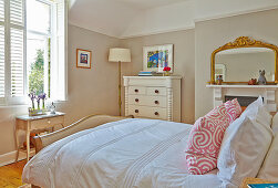 Double bed, white dresser and fireplace with mirror in the bedroom
