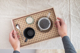 Eine Kanne Tee, Becher und Milch auf DIY-Tablett mit Wiener Geflecht