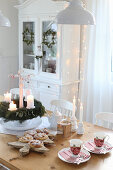 Adventskranz, Apfelschnecken, Kerzen und Tassen auf Weihnachtstisch