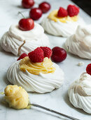 Individual meringues topped with lemon curd, raspberries, whipped cream and cherries