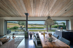 Esstisch aus Holz in offenem Wohnraum mit Glasschiebetür, Blick auf Pool und Landschaft