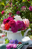 Bouquet of roses in enamelled jug, rose petals, strawberry and cranesbill flowers on napkin