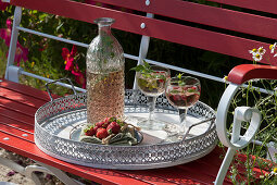 Bottle, glasses of strawberries and mint and plate of strawberries on tray
