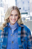A young blonde woman wearing blue denim dungarees and a checked jacket