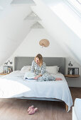 Blonde woman sitting with book on bed in attic room
