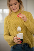 Blonde woman holds a tea bag in a mug