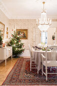 Festively set Christmas table in beige, chandelier above, Christmas tree in corner of room