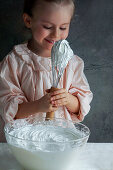 Little smilling girl prepares whipped cream and tastes it straight from the whisk