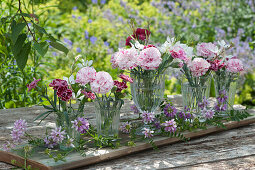 Kleine Sträuße aus Nelkenblüten und Prachtkerzen als Tischdeko auf ein Brett gestellt und mit Ranken von Kronwicke dekoriert