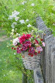 Small bouquet with carnations and wild strawberries in a hanging basket on the fence