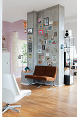 Pictures, photos and decorative letters on concrete partition with brown armchairs below in open-plan interior