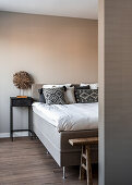 Double bed, bedside table and rustic bench in bedroom with pale painted wall