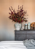 Vintage vase of autumn branches on dresser against pale painted wall