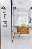 Shower area in the bathroom with marble tiles, wooden counter with a vessel sink in the background