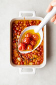 A white spoon filled with just-cooked tomato confit and olive oil