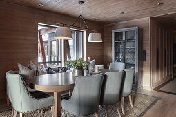 Oval dining table with grey upholstered chairs in elegant dining room with wood panelling