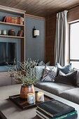 Coffee table, sofa with scatter cushions and custom shelves in room with grey wall and wooden ceiling