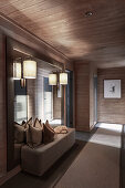 Upholstered bench below mirror on in elegant, illuminated hallway with wooden panelling