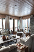 Elegantes Wohnzimmer mit grauen Polstermöbeln, Fenstern, bodenlangen Vorhängen und Holzverkleidung