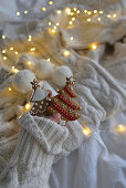 Gingerbread fir tree with fairy lights and pompoms on a white knitted blanket