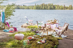 Barbecue and various chairs around festively set table by a lake