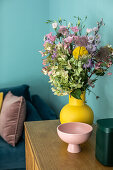 Lowboard with bouquet of flowers and bowl in front of blue wall