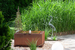Square water feature made of Corten steel in a gravel bed, metal crane, climbing stele, Chinese reed as a privacy hedge on the terrace