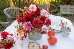 Dahlienstrauß mit Hagebutten und Herbstlaub als Tischdekoration, Kürbisse, Apfel und Geschirr