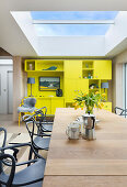 Wooden table and classic chairs under skylight and lime-green fitted cabinets in open-plan interior