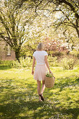 Blonde Frau in weißem T-Shirt und Rock mit Blumenkorb im frühlingshaften Garten