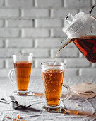 Pouring rooibos tea from a glass jug into a tea mug