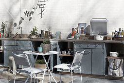 Filigraner Tisch mit Stühlen vor Outdoorküche aus verzinktem Stahl