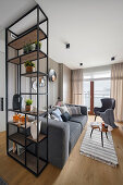 Grey upholstered sofa, coffee table and armchair in open-plan interior with shelving used as room divider