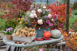 Autumn terrace: autumn bouquet with roses, rose hips, chrysanthemums and autumn asters, basket with chestnuts, pumpkins, chillies, rose hips and pansies