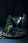 Martini cocktail with rosmary sprigs, olives and pistachios