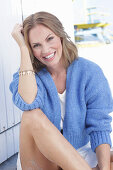 Long haired woman in white summer dress and blue cardigan sitting on the beach