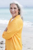 Reife Frau mit grauen Haaren in orangefarbener Bluse am Strand