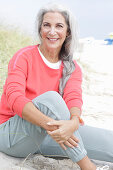 Mature woman with grey hair in salmon-coloured jumper and trousers on the beach