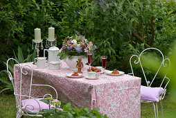 Romantic coffee table in May set with a bouquet of wildflowers, sparkling wine, strawberries, strawberry tartlets and coffee set