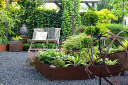 Raised bed and decorative ball made of Corten steel, wooden bench in the background