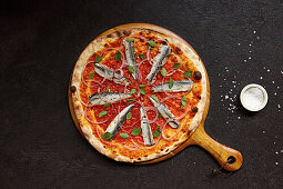 Pizza mit frischen Sardellen, roten Zwiebeln, Oregano und getrockneten Chiliflocken