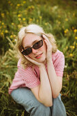 Junge blonde Frau mit Sonnenbrille sitzt auf einer sommerlichen Blumenwiese