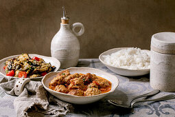 Dinner with marinated eggplants, meatballs in tomato sauce and boiled rice in white ceramic plates.