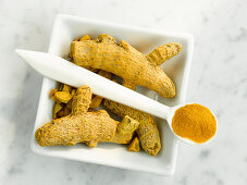 A bowl with turmeric root and a spoon with turmeric powder