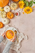 Bowl of pumpkin soup on table with vegetables and sunflowers in light kitchen