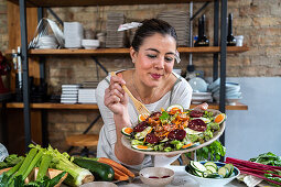 Adult content female with delicious vegetable salad on plate and wooden fork at table against brick wall