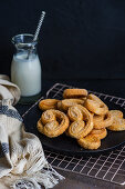 Schweinsöhrchen aus Blätterteig auf dunklem Teller dazu eine Flasche Milch